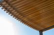 Minimalist sunshade design made of wooden slats for architecture projects. Wooden pergola canopy with beams against blue sky, modern outdoor structure.
