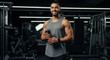 © Milan - Smiling muscular man holding a protein shaker bottle in a modern gym. Fit athlete resting after a workout.
