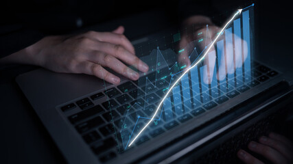 Close-up of hands using a laptop with digital graphs displayed above the keyboard, symbolizing data analysis and business growth in a modern setting. Impute