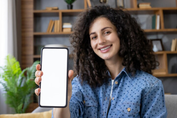 Smiling woman showing smartphone with blank screen at home