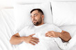 © Prostock-studio - Peaceful calm tired millennial caucasian muscular man lies on white comfortable bed, soft pillow, sleeps alone in bedroom, top view. Facial expression, night healthy sleep, rest and relaxation at home