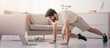 © Prostock-studio - Sports at home, online lesson and body care during self-isolation. Serious arabian bearded young guy doing exercises for legs looking at laptop with dumbbells, bottle of water on floor in living room