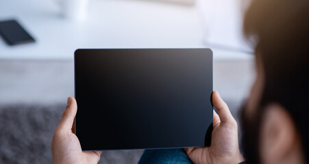 Unrecognizable guy using digital tablet with empty screen, browsing internet or showing new app, sitting on floor at home. Website advertisement concept. Rear view, mockup