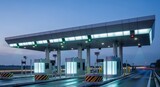Modern illuminated highway toll plaza at dusk with wet road reflections. Efficient transportation infrastructure and traffic management system.