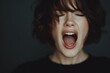 © Nanda - Woman with short brown hair screams with eyes closed in dark studio. Use this for projects about stress, sadness, or mental health concepts.