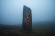 © MINK - Mysterious monolith covered in glowing symbols stands in a misty field, invoking a sense of ancient technology