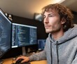© Basileus - A focused programmer intently examines lines of code on multiple computer screens.