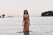 © SHOTPRIME STUDIO - A model stands in shallow sea water wearing a silky brown dress, calm expression, soft lighting, gentle waves, distant horizon, creating a serene coastal portrait.
