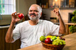 © StockImageFactory - Indian Old man enjoying apple and urging healthy eating from home kitchen