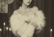 © kharchenkoirina - sepia color black and white film old style photo real person retro lady roaring sexy woman. Flapper girl in room 20s. Close-up portrait make-up face lips, cape boa fur fox pearls on shoulders 1920s