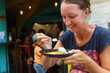 A woman enjoys a delightful dish of Thai street food during a lively evening with vibrant surroundings and happy diners.