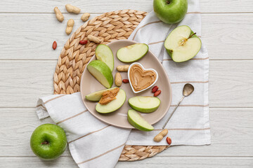 Wall Mural - Plate with fresh apple slices and bowl of sweet peanut butter on white wooden background