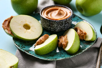 Wall Mural - Plate of fresh apple slices with sweet peanut butter on blue background, closeup