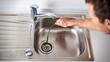 © Varos - A hand uses a plumbing snake to clear a clogged drain in a white sink, illustrating home maintenance, repair, and problem-solving. Ideal for DIY, plumbing services, and household repair concepts.