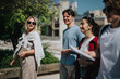 © qunica.com - A group of happy students engaged in conversation while walking in a sunny outdoor setting. Their expressions exhibit joy and camaraderie, and the background suggests a campus or urban environment.