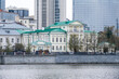 Historic government building with green roof on embankment of the Iset River in Yekaterinburg, contrasted with modern glass skyscrapers in the background