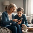 © Arie - Grandmother and grandson looking at smartphone screen indoors cozy living room modern technology family time