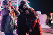 © qunica.com - Close group of friends enjoying a fun-filled evening, sharing smiles and warmth at an outdoor nighttime festival, surrounded by colorful lights and cheerful ambiance.