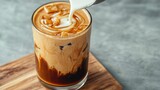 Delicious iced coffee with milk pouring in a glass on a wooden surface with natural texture and beautiful colors