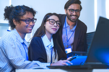A happy and diverse tech team celebrates a successful project outcome. Smiling colleagues, led by their manager, look at the results on a computer in a modern office.