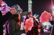 © qunica.com - A group of friends having fun sharing cotton candy at a vibrant carnival during nighttime, with colorful lights and cheerful ambience enhancing the festive and cheerful atmosphere.