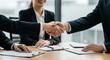 © Alexandre - Business people shaking hands over a table with documents during a meeting in an office space
