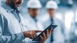 © Thares2020 - Professional engineer utilizes a digital tablet for planning and data analysis with colleagues in safety gear observing in a modern industrial