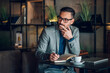 © Zamrznuti tonovi - Businessman thinking and taking notes in cafe with laptop and coffee