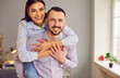 © Studio Romantic - Loving couple, portrait of smiling husband piggy backing beautiful wife, having fun, overjoyed young couple hugging, looking at camera, enjoying leisure time at home together in romantic relationships