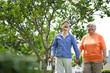 © JU.STOCKER - Happy senior Asian couple holding hands while walking in park, Joyful elderly man and woman enjoying a stroll together, Cheerful mature couple laughing during a leisurely outdoor walk