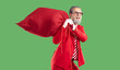 © Studio Romantic - Modern, extravagant, young Santa Claus in red business suit screams with joy and happiness with huge, red bag filled with gifts on isolated green background. Christmas gift delivery.