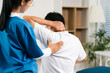 © NINENII - senior man doing exercise at clinic with physiotherapist. help of a personal trainer during a rehabilitation session.