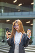 © maeching - Asian businesswoman in suit using mobile phone while standing in front of modern business building.