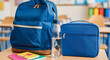 © abu - Back-to-school set with backpack, water bottle, and lunch bag in classroom.