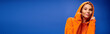 © LIGHTFIELD STUDIOS - Trendy young woman strikes a fun pose in an orange hoodie in a vibrant studio