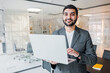© muse studio - Professional man in smart suit confidently presenting laptop in modern office environment