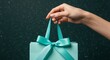 © purple - Delicate Teal Gift Bag Held by a Hand Against a Dark Background