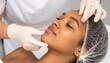 © photostockatinat - A close-up shot of a dermatologist examining a patient's face. The dermatologist is wearing gloves and the patient is in a medical head covering