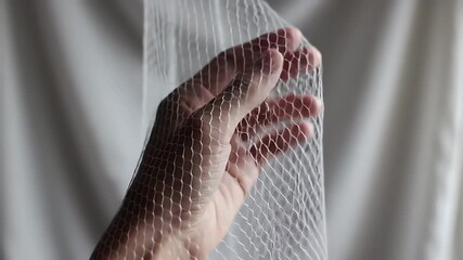 Hand Tilting Mesh Fabric in Gentle Upward Motion Against Soft White Backdrop Studio Close Up Subtle Movement Playful Light and Shadow Texture Focus Abstract Conceptual