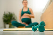 © Sk Elena - Dumbbells in focus, pregnant woman stretching or doing yoga in the background. Calm fitness routine during pregnancy.