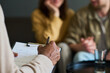 © pressmaster - Middle aged Black man holding clipboard and pen conducting counseling session with young Caucasian couple sitting together in background, couple holding hands and listening attentively