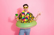 © deagreez - Young man in a tropical outfit with inflatable ring enjoying vacation and pointing at something on a pink background