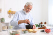 © New Africa - Elderly man cooking at white marble table in kitchen