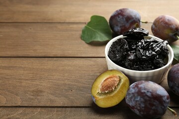 Wall Mural - Dried prunes, fresh plums and green leaves on wooden table, closeup. Space for text