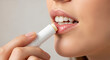 © ArtFocus Studio - Woman applying lip balm on light background. Close-up studio shot of healthy, glossy lips. Moisturizing treatment, everyday beauty routine.