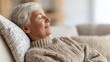 © Marina - Relaxed older woman enjoying peaceful moment on cozy sofa, exudi