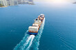 Big heavy container ship leaves the bay and strait for the open ocean near a metropolis with multi-story buildings