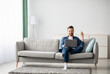 © Prostock-studio - Relaxed middle-aged man with laptop sitting on couch at home, surfing on Internet or watching movie, raising hand with AC remote up, copy space. Cooling systems for home, air conditioner concept