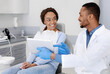 © Prostock-studio - Cheery african guy dentist showing woman patient his clinic website on digital tablet
