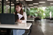 © snowing12 - Asian woman freelancer works on laptop outdoors reviewing business report digital nomad lifestyle remote worker in modern open space productive work